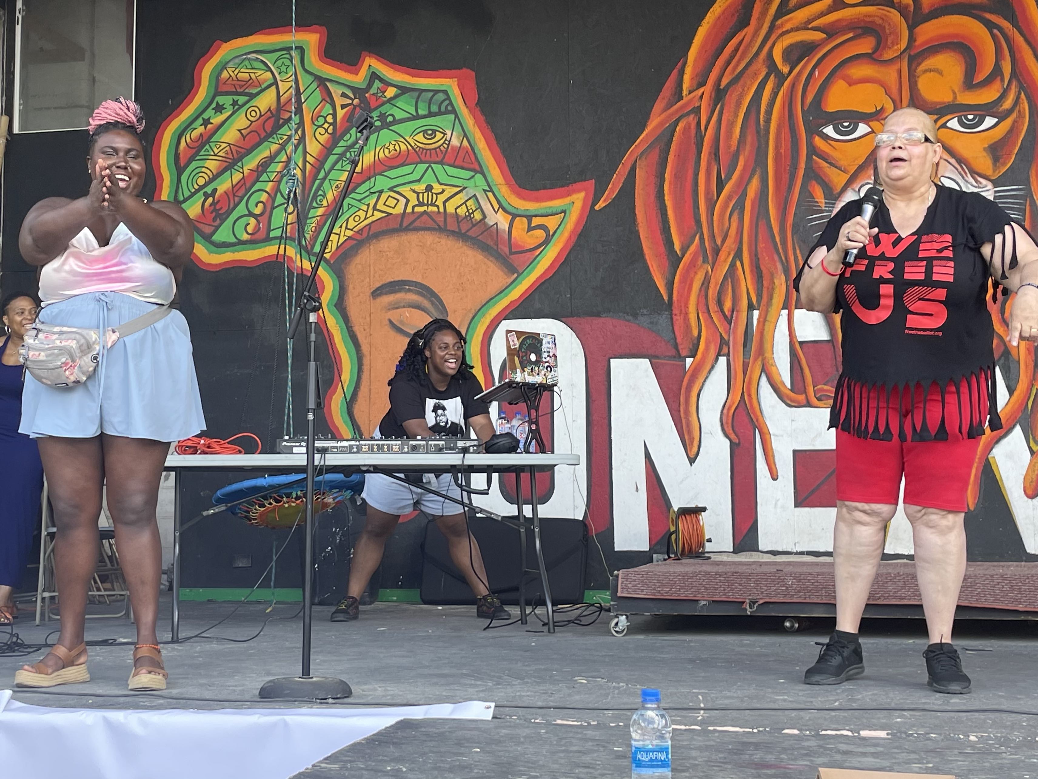 Mrs Dee Dee and Nikki Grant stand on the stage as DJ Ansharay spins records