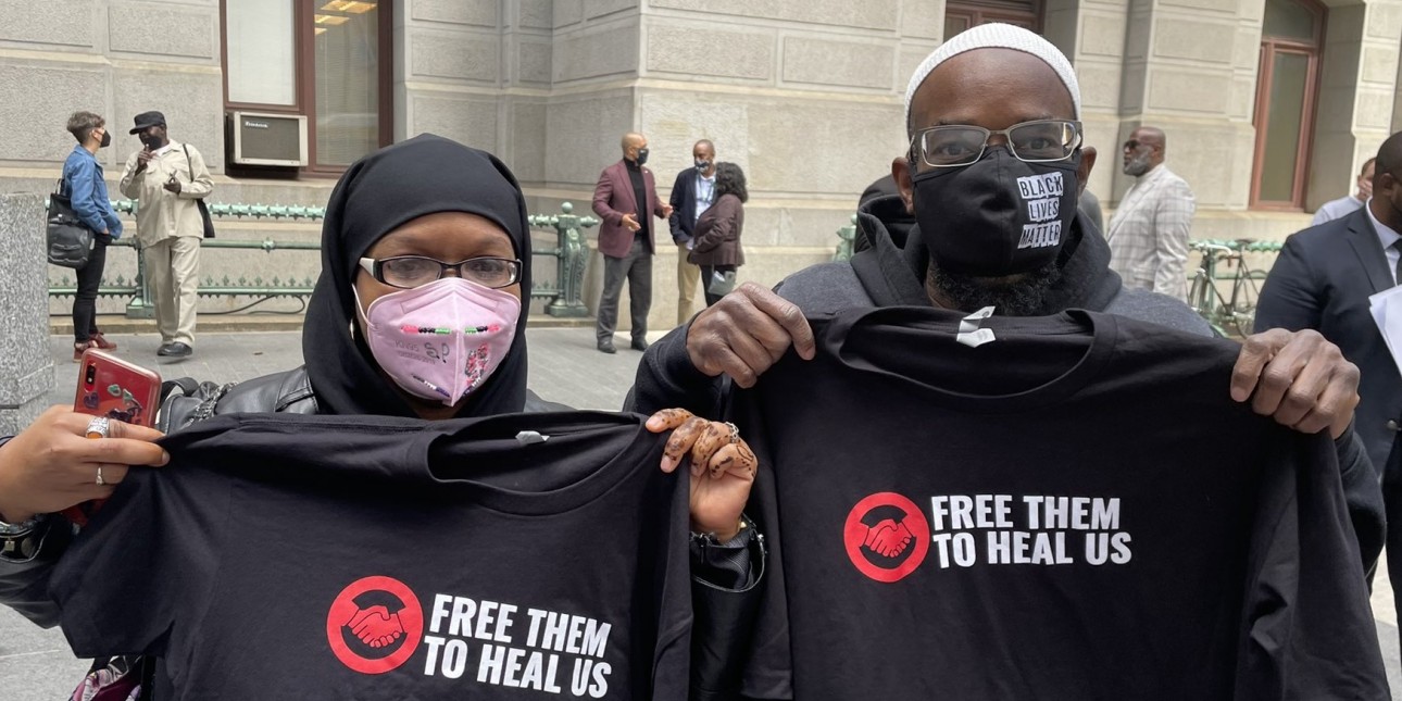 A man and a woman stand next to each other holding up shirts that say 'Free Them to Heal Us' 