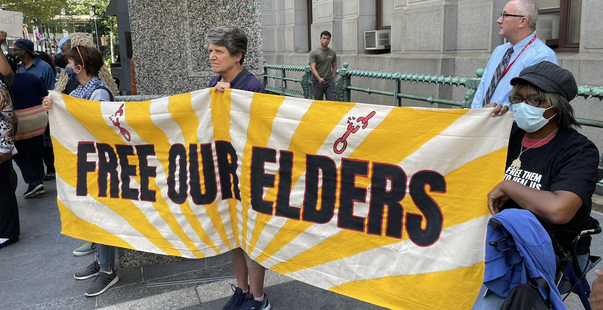 People hold a yellow banner that reads 'Free Our Elders' 