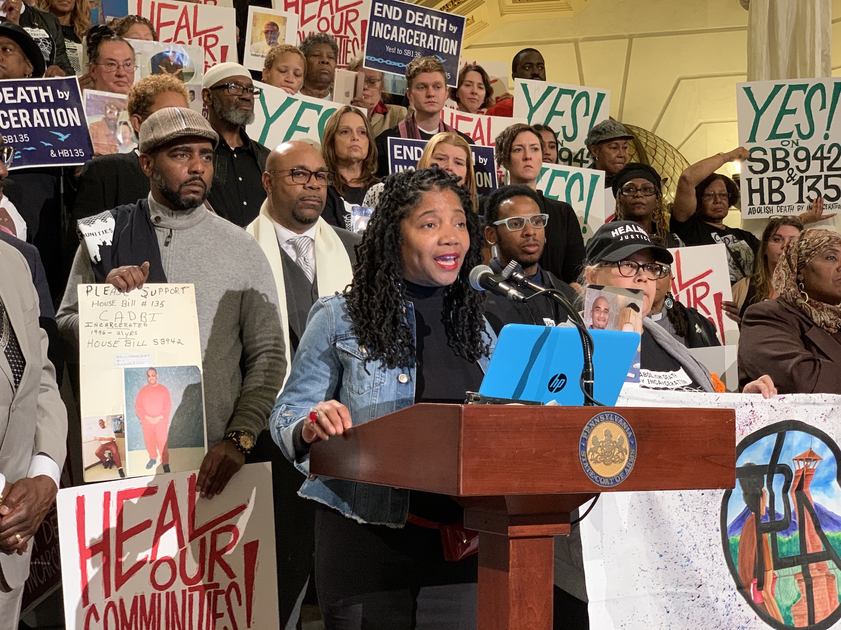 Kim King speaks at a rally with a crowd gathered behind her holding signs against death by incarceration