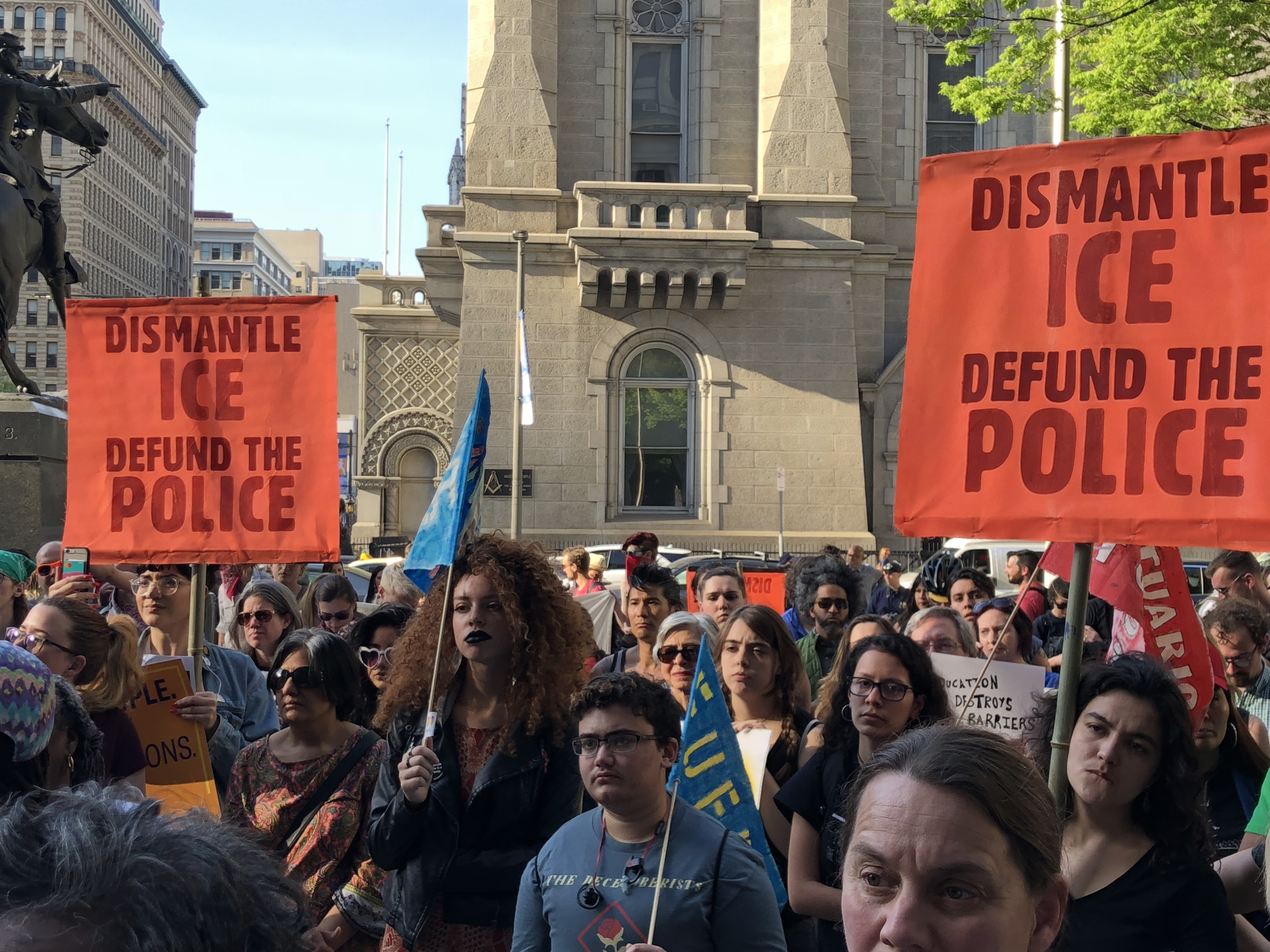 People gather at a protest with banners that read 'Dismantle Ice, Defund the Police'