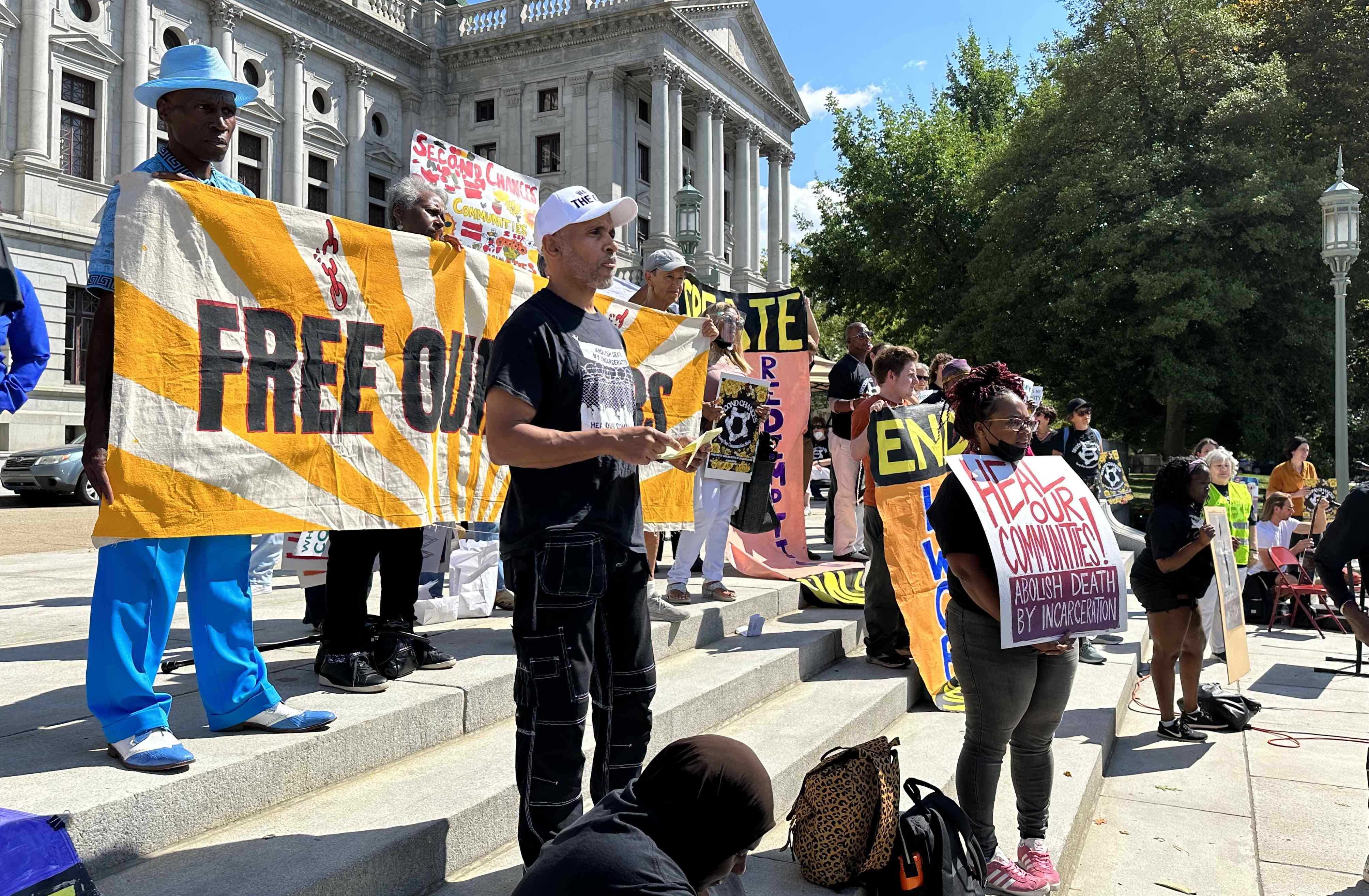 People gather in front of a yellow banner that reads 'Free Our Elders