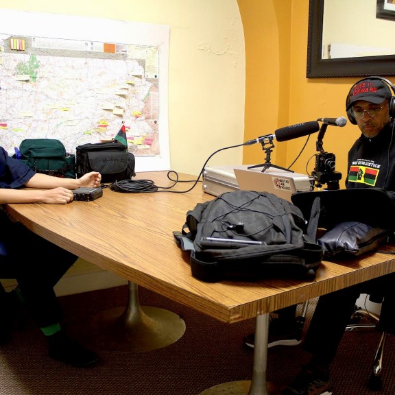 Ghani sits in front of the mic while Kyla records him.