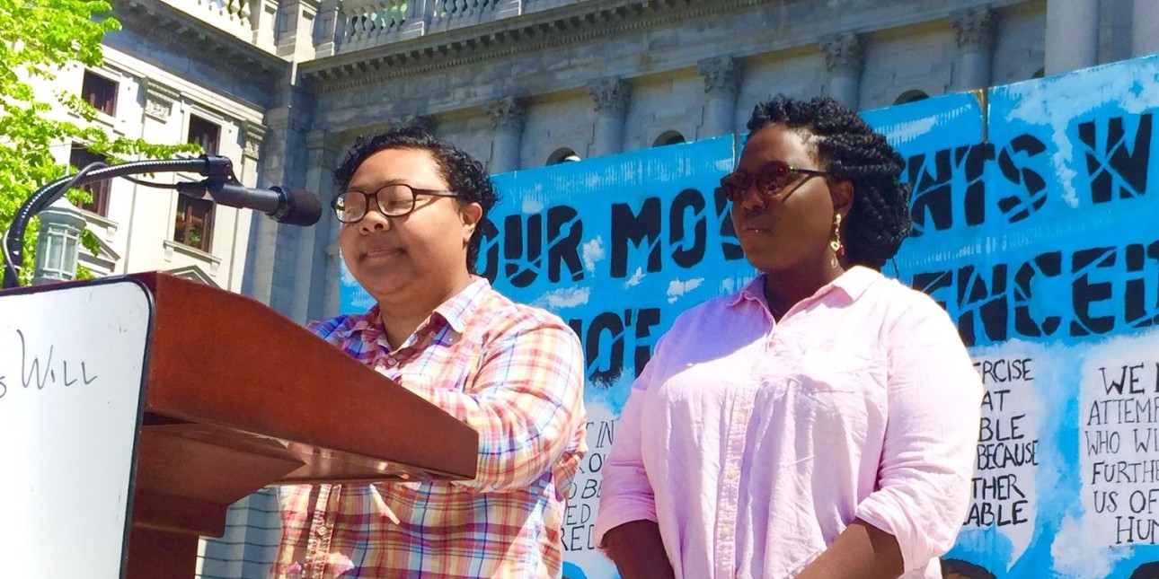 a picture shows Kris Henderson speaking at a a podium at a rally next to Nikki Grant