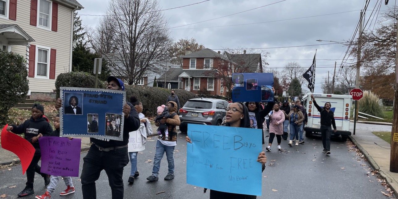 an image shows members of Angelo Strand's family marching with signs saying 'Free Big Yo' 