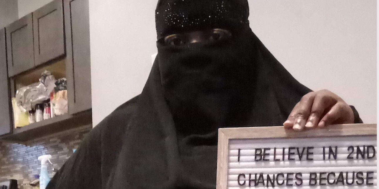 A woman in a burka holds a cellphone with a picture of her loved one in prison and a sign that says 'I believe in 2nd chances because when family is locked up a part of you r locked 2'