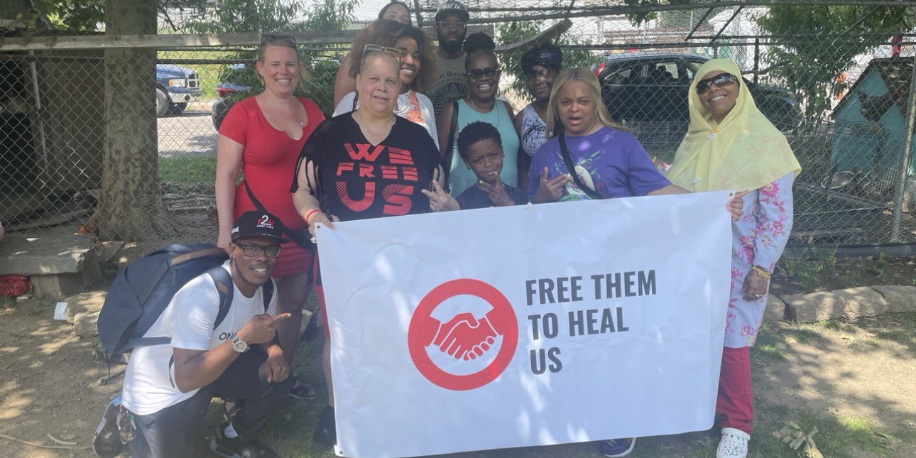 A group of people stand behind a banner that reads Free Them to Heal Us