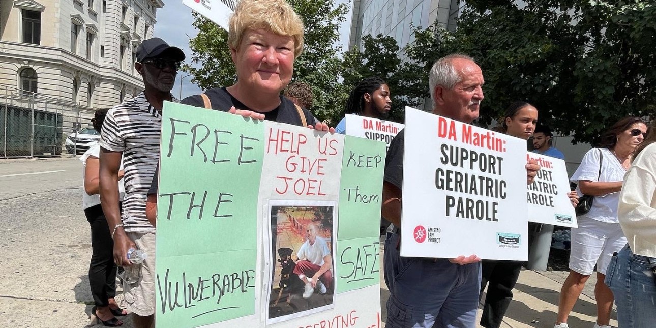 A crowd huddles together and holds signs that read "DA Martin - Support Geriatric Parole'