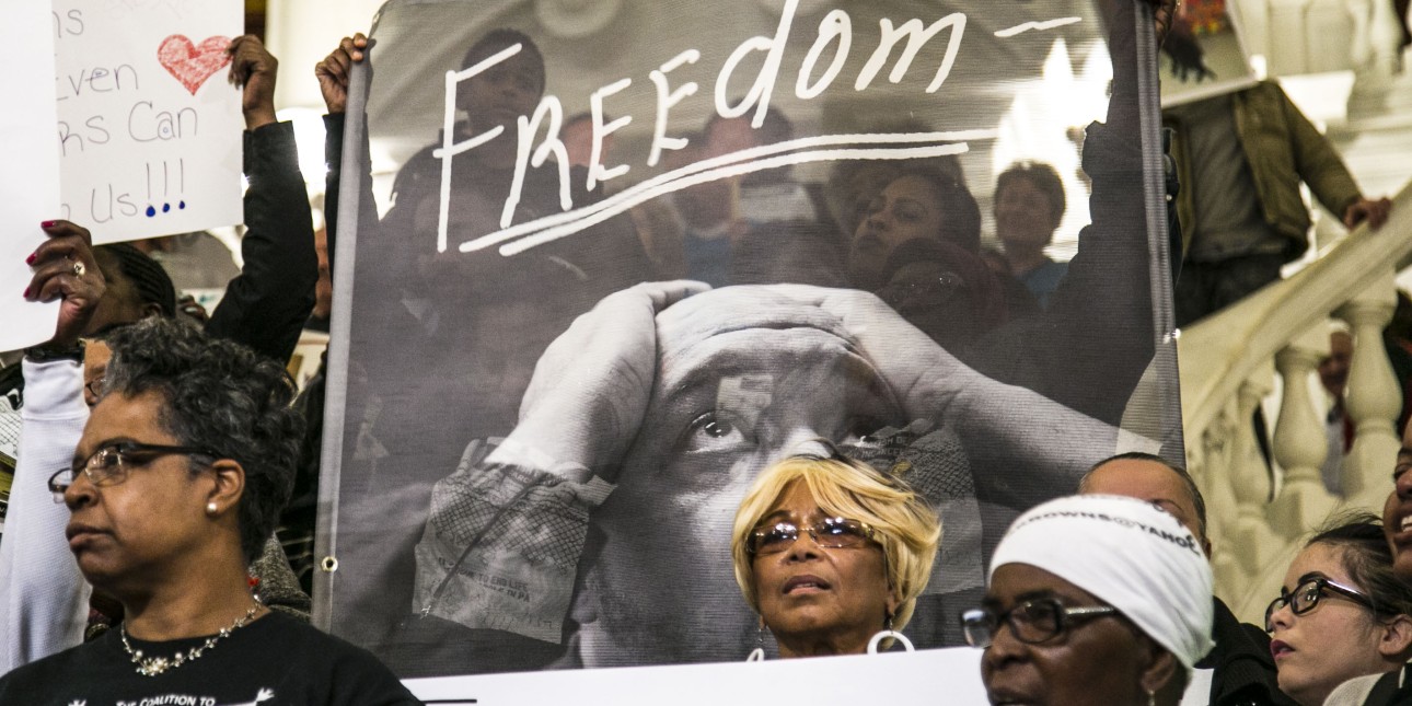 people at a rally stand in front of a banner that reads 'freedom'