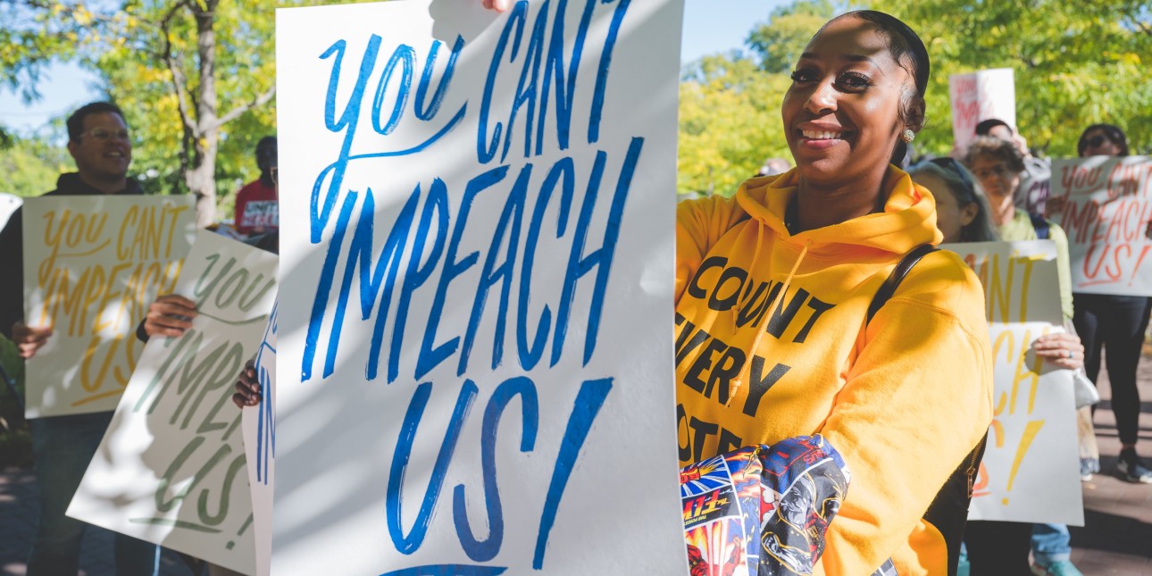 a woman smile into the camera holding a you can't impeach us sign
