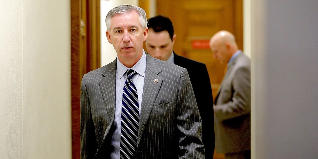 DA Kevin Steele wears a grey suit and walks toward the camera