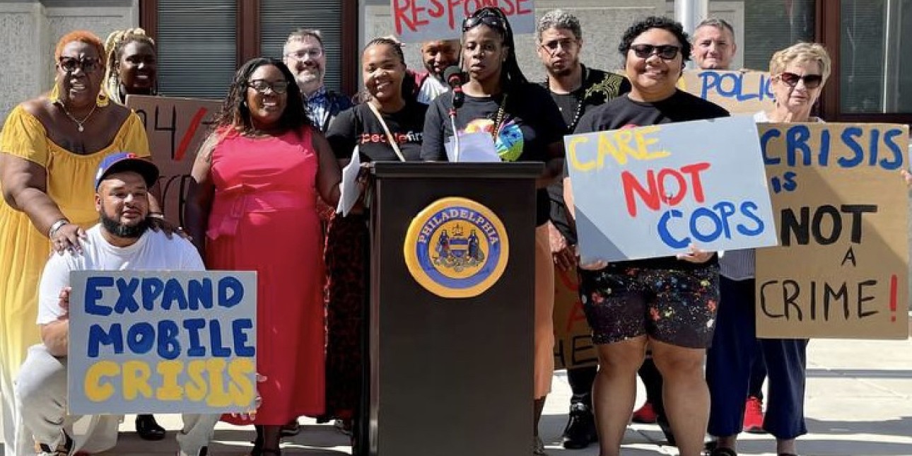 a group of people gathers around holding signs that say 'expand mobile crisis' 'care not cops' and 'crisis is not a crime' 