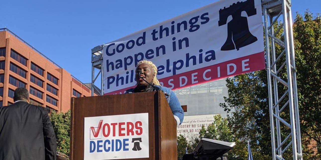 Nikki Grant speaks at a podium with a sign on it that says Voters Decide