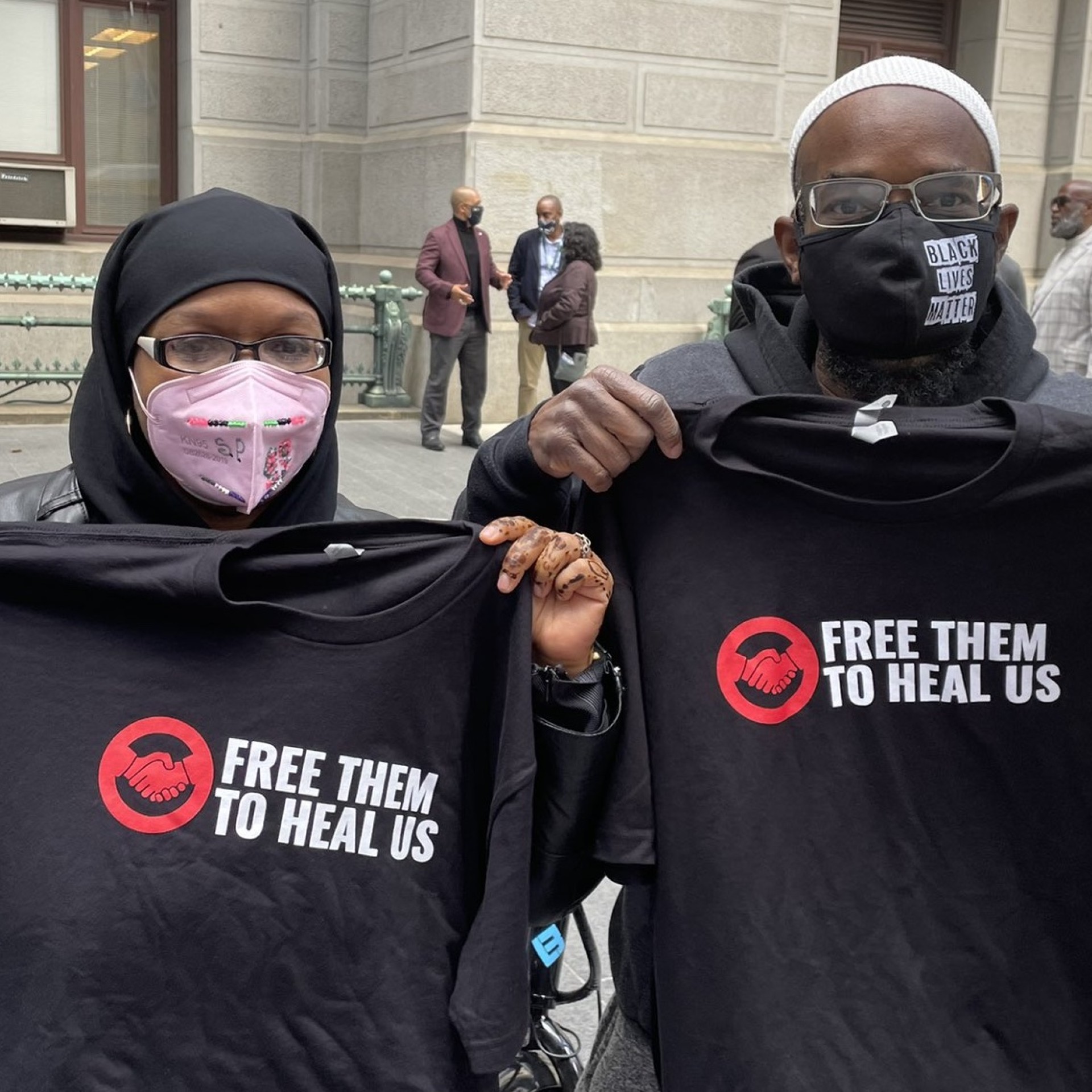 Two members of Free Them to Heal Us hold t-shirts with the Free Them to Heal Us logo displayed