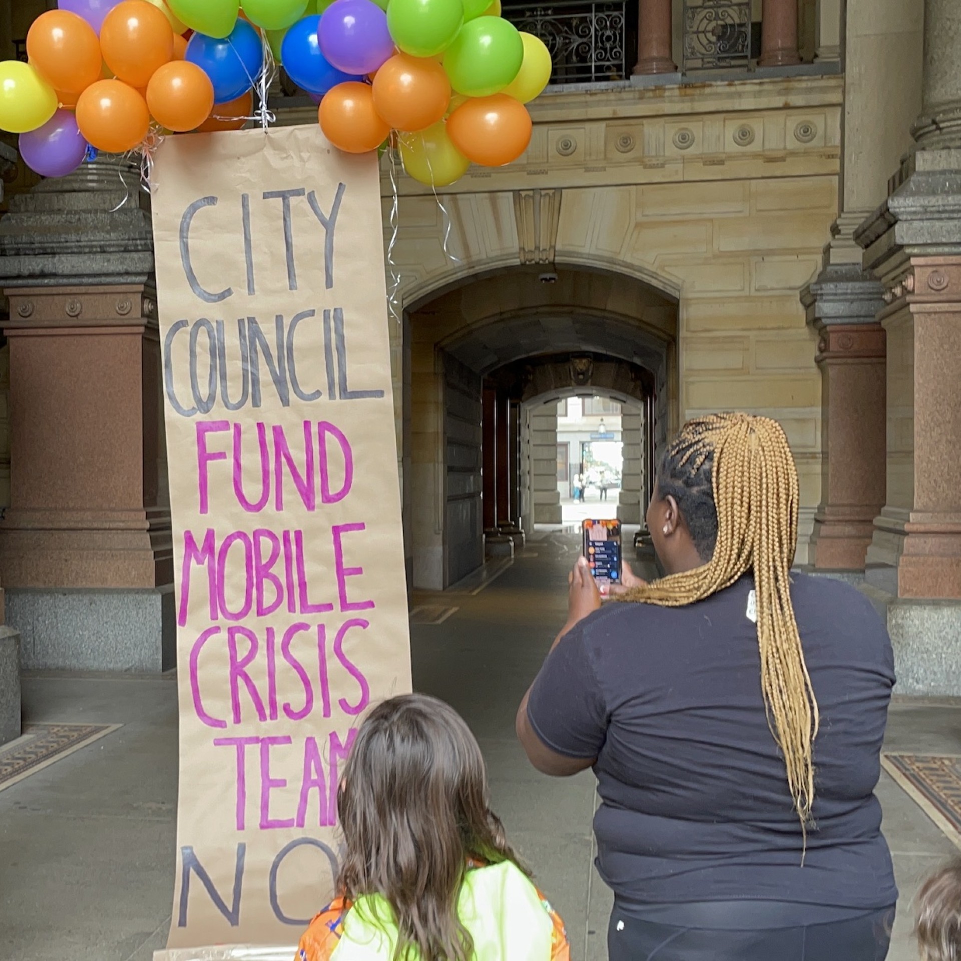 an image shows a balloon banner that reads 'city council fund mobile crisis teams;