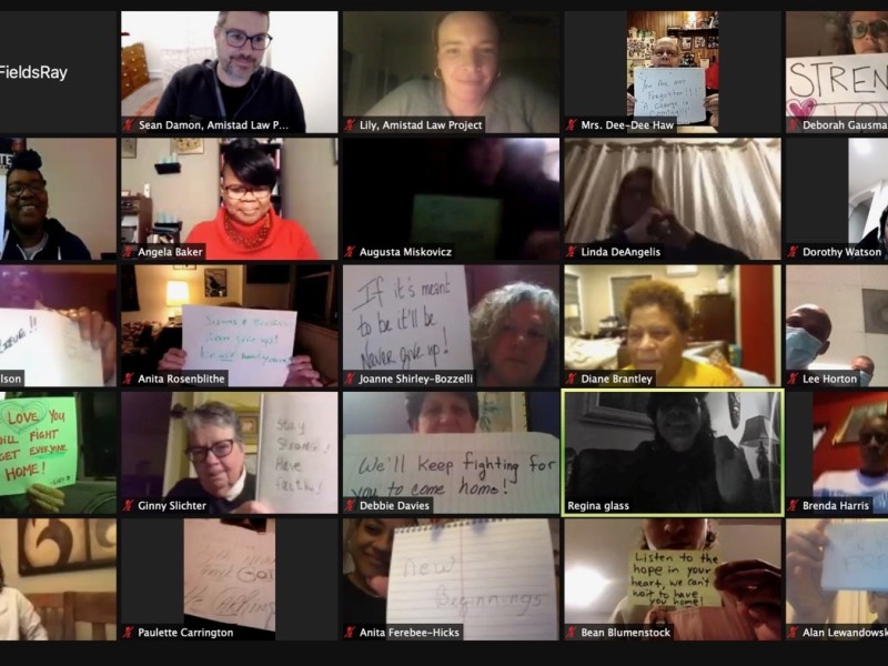 A screenshot of a zoom meeting shows people holding up signs with messages of hope and liberation