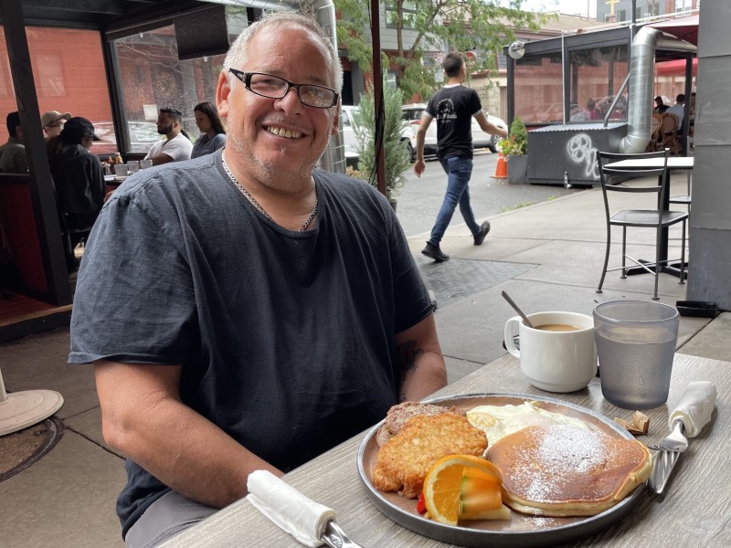 Francisco Mojica sits at a table front of a breakfast plate with eggs and pancakes. 