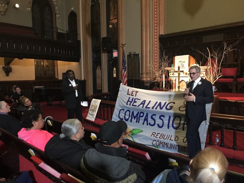 Larry Krasner stands in front of a banner that reads 'Healing and Compassion' in front of a mostly Black audience. 