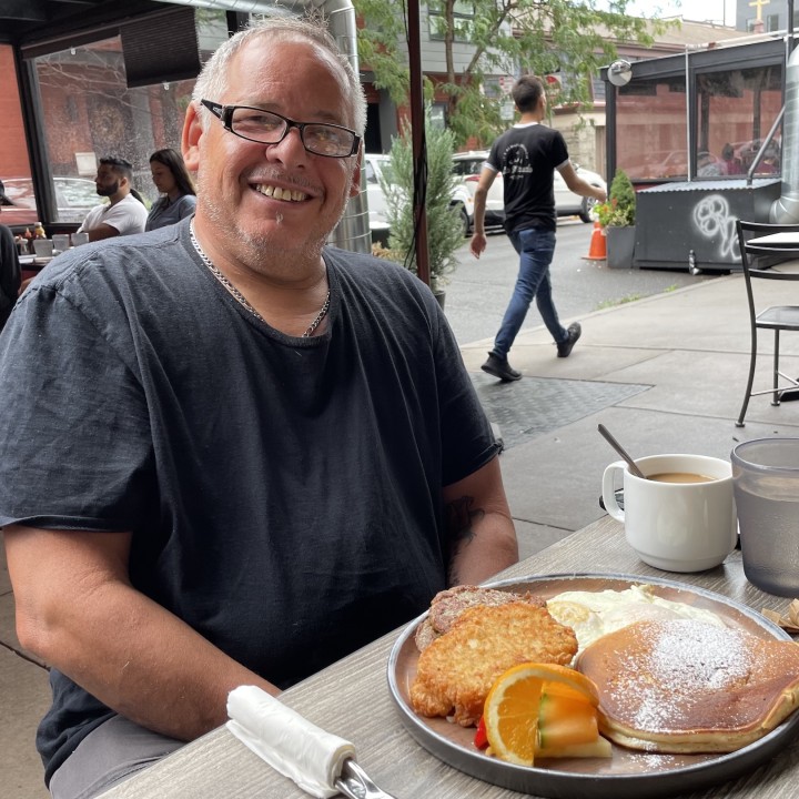 Francisco Mojica sits at a table front of a breakfast plate with eggs and pancakes. 
