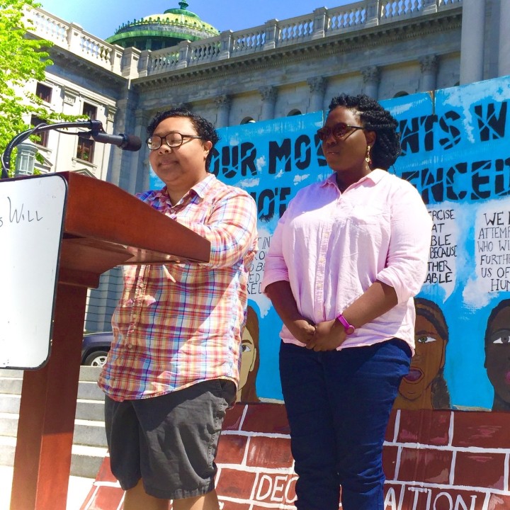 a picture shows Kris Henderson speaking at a a podium at a rally next to Nikki Grant