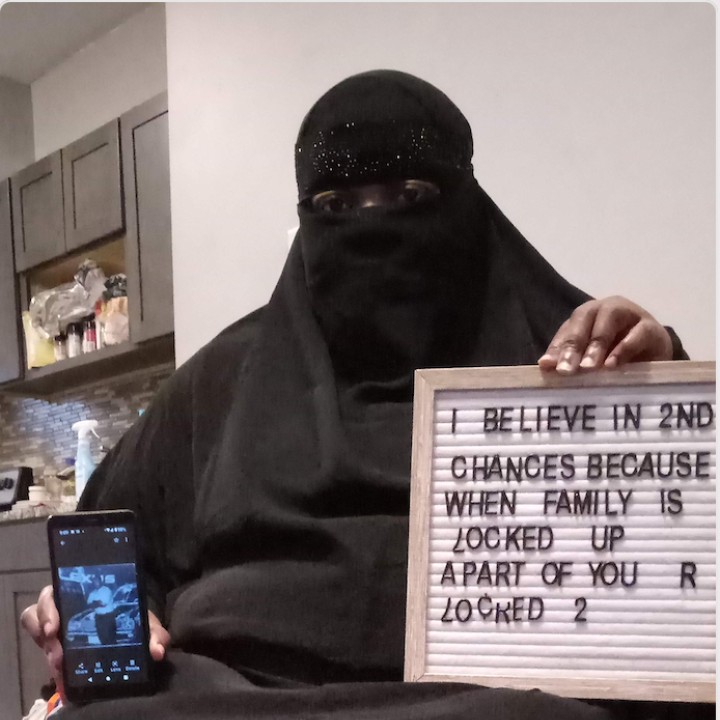 A woman in a burka holds a cellphone with a picture of her loved one in prison and a sign that says 'I believe in 2nd chances because when family is locked up a part of you r locked 2'