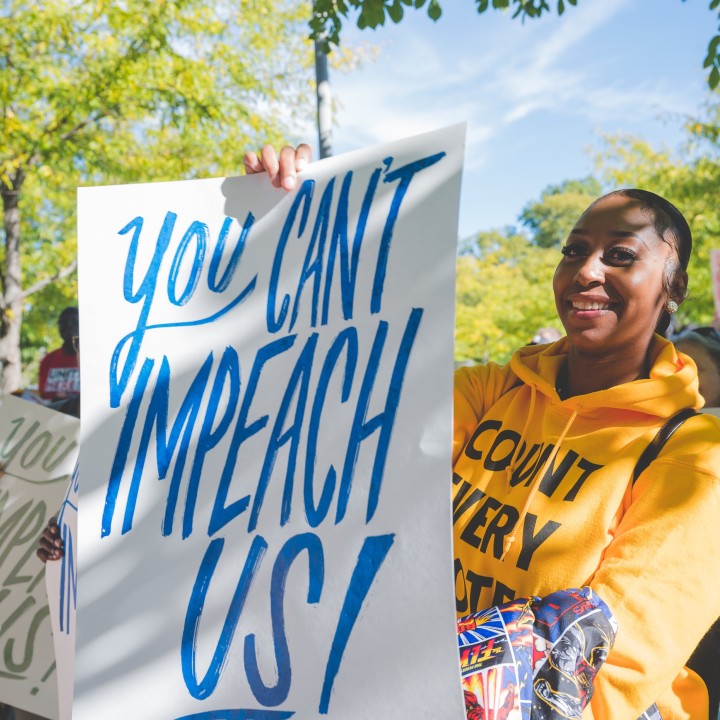 a woman smile into the camera holding a you can't impeach us sign